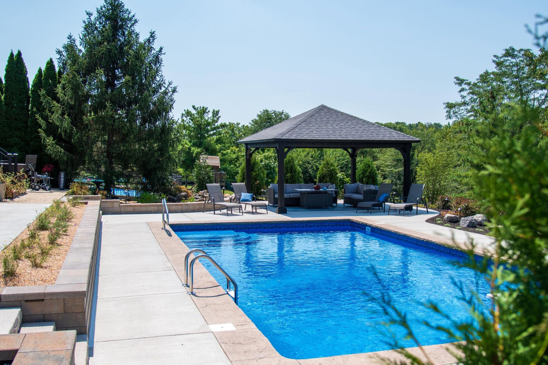 Pool surrounded by mature plantings, retaining walls, and a shaded pavilion